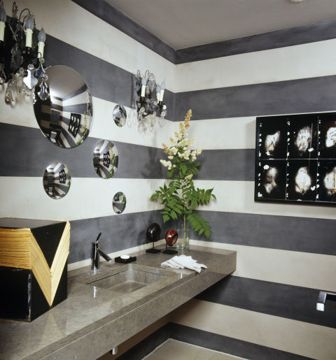 Alternating stripes of gray and white paint enliven the powder room of a modernist home in Geneva, which was decorated by Alexandra de Garidel-Thoron of the Swiss design studio Thébaïde. A constellation of convex mirrors appears to float above the stone sink.