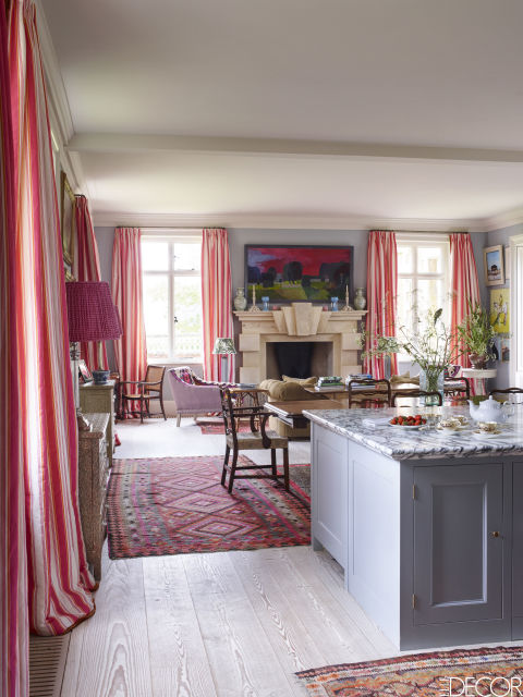 The living room in this English country house features curtains of a Bennison Fabrics stripe, walls painted in Tablecloth by Paint & Paper Library and 2015 artwork above the mantel by Fred Ingrams.