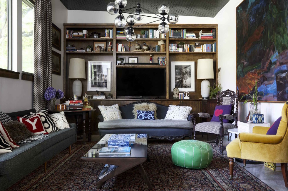 In the living room of designer Erika Yeaman's home, Scandinavian influences such as the warm wood bookshelf and matte black chandelier are accented by colorful bohemian pillows. 